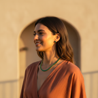 Woman wearing a green necklace in front of a beige wall with an arch
