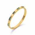 Gold bracelet with emerald green stones on a white background