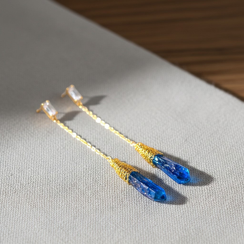 The Accessory Bar gold-plated drop earrings featuring blue crystal pendants and bezel-set cubic zirconia studs.