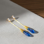 The Accessory Bar gold-plated drop earrings featuring blue crystal pendants and bezel-set cubic zirconia studs.