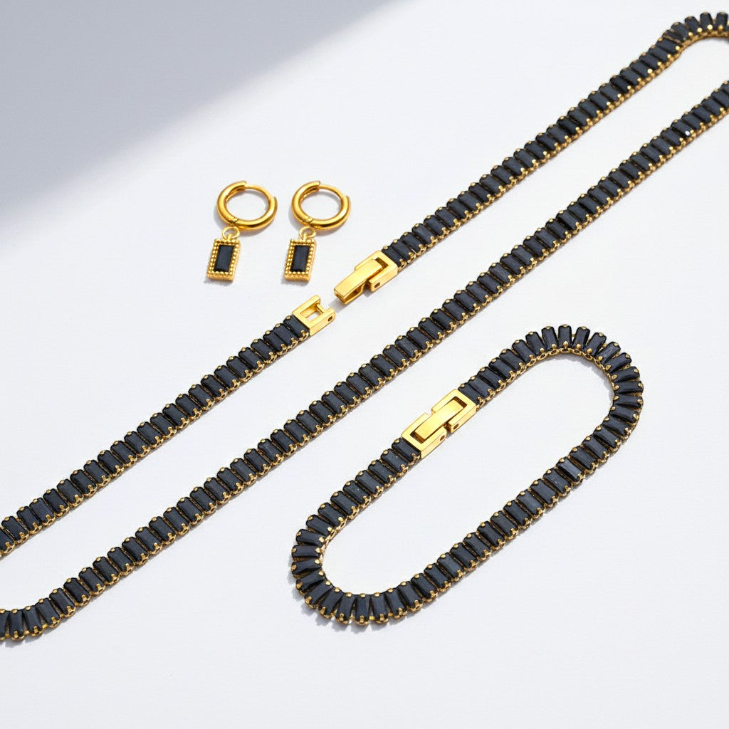 The Accessory Bar Leila set featuring a gold-tone stainless steel tennis necklace, bracelet, and black stud earrings.
