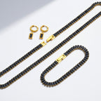 The Accessory Bar Leila set featuring a gold-tone stainless steel tennis necklace, bracelet, and black stud earrings.
