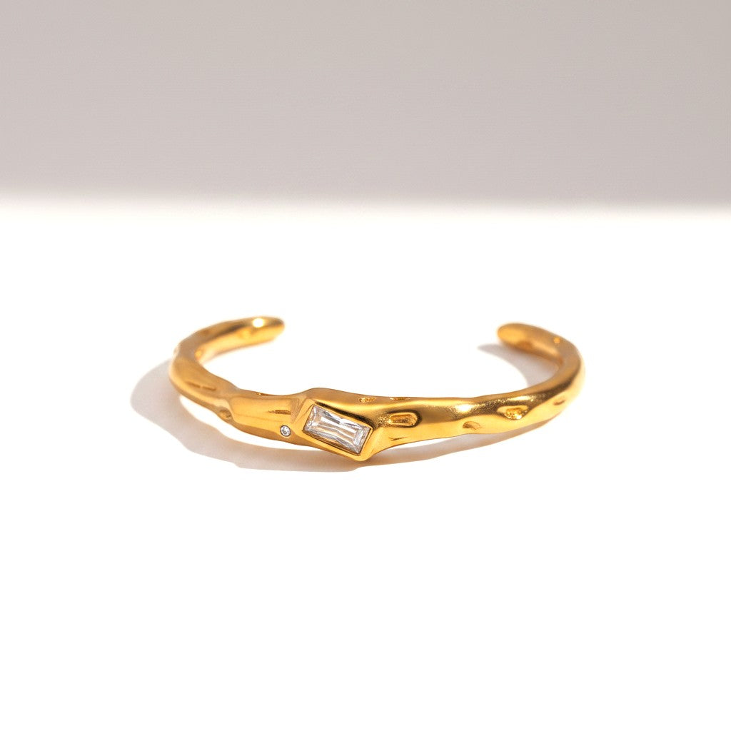 The Accessory Bar Lina gold-plated open cuff bracelet with a central bezel-set baguette cubic zirconia stone.