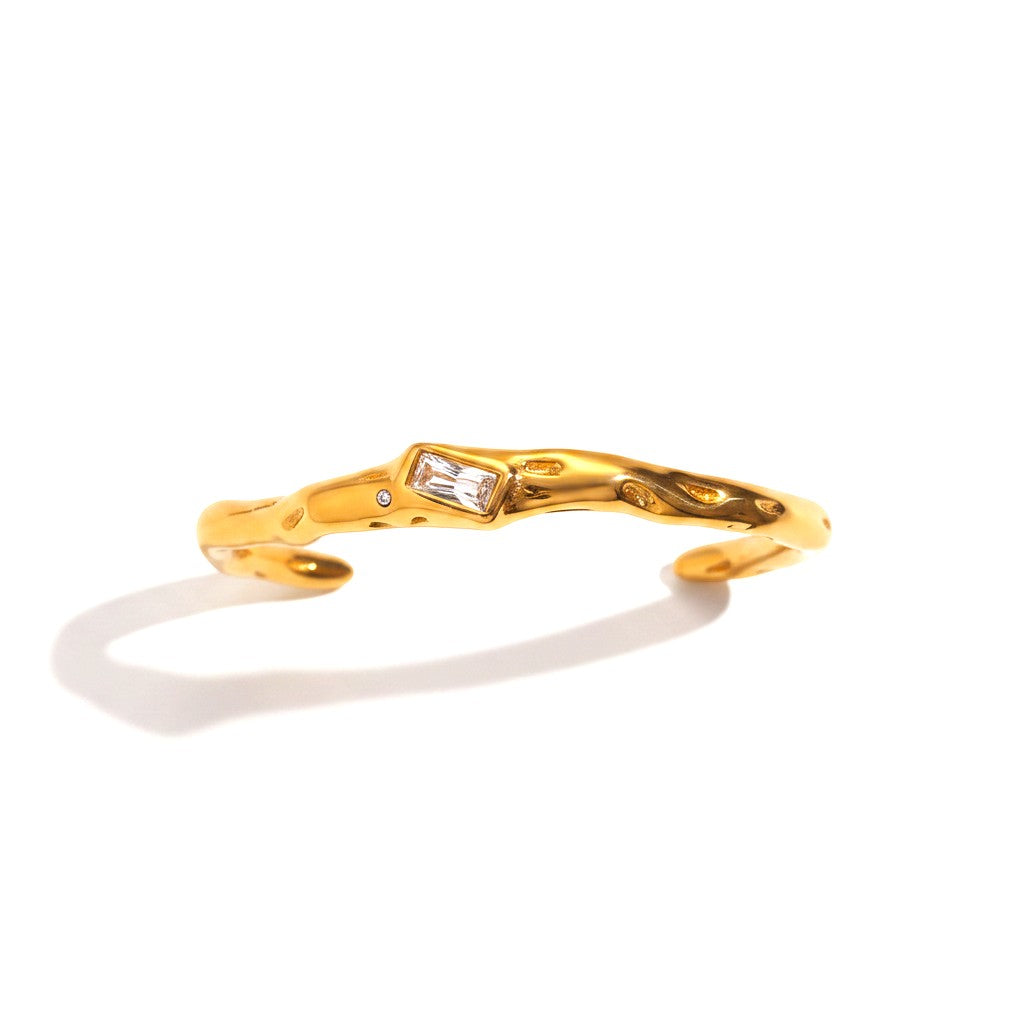 The Accessory Bar Lina gold-plated open cuff bracelet with a central baguette-cut white cubic zirconia stone.