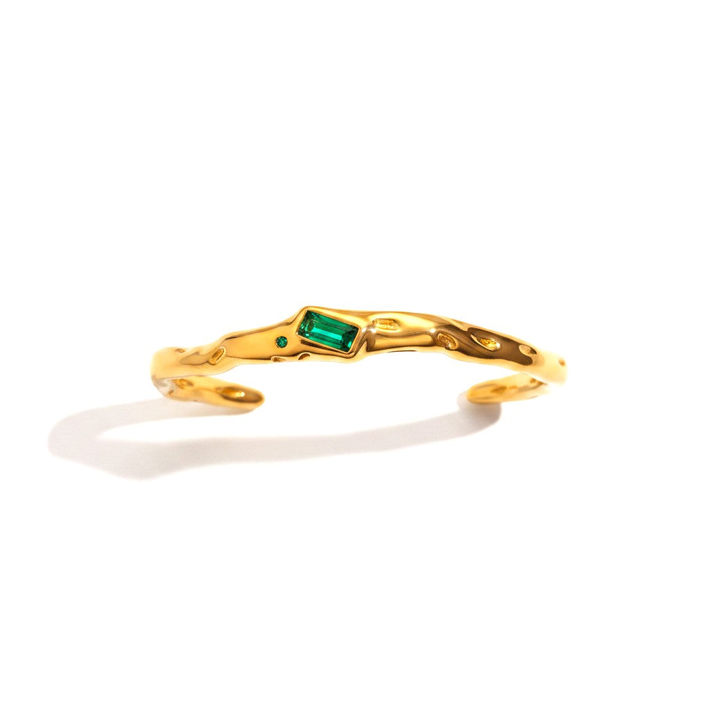 The Accessory Bar Lina open cuff bracelet in PVD gold-plated stainless steel with a bezel-set emerald green stone.