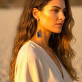 Model wearing The Accessory Bar gold-plated pendant earrings with blue crystal drops and cubic zirconia accents.
