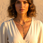 The Accessory Bar Yara lariat necklace with green and clear cubic zirconia on a model in a white dress at sunset.